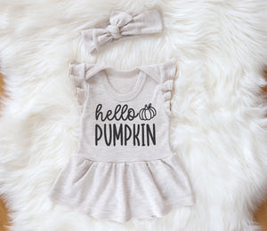 heather beige fall baby girl bodysuit dress with flutter sleeves and heather beige knot headband made of 100 percent cotton. On the front of the dress there is a print that says 'hello pumpkin' in black color. The outfit is photographed laid down on a white fur backdrop.
